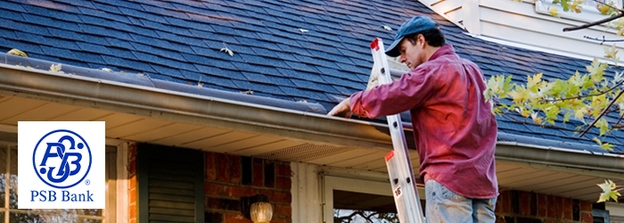 Man on ladder clearing leaves out of the gutter of his house