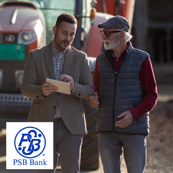 Farmer and banker looking at information on tablet while walking outside past farm equipment