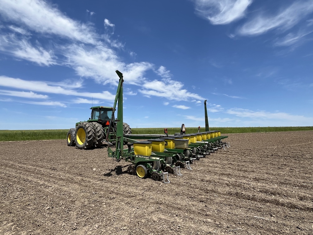 Tractor and row planter in a freshly prepared agricultural field under a blue sky.