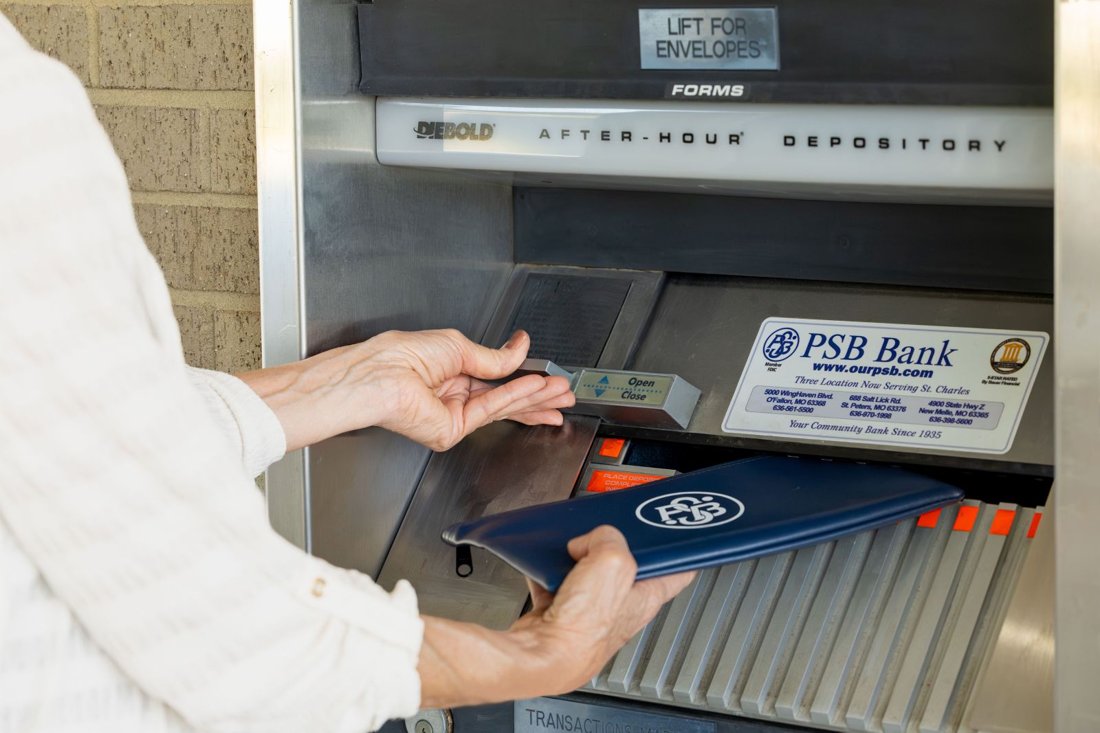 Person using a PSB Bank after-hours depository while holding a PSB Bank deposit bag.