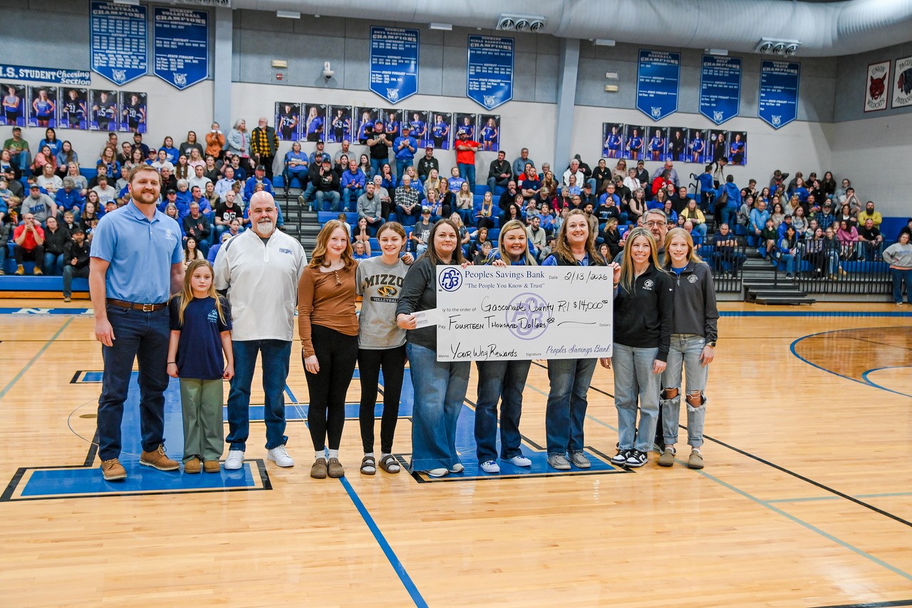 PSB Bank representatives present a $14,000 Your Way Rewards donation check to Gasconade County R-I School District during a basketball game in a packed school gymnasium. Students, school staff, and bank employees stand together at center court while community members watch from the bleachers.