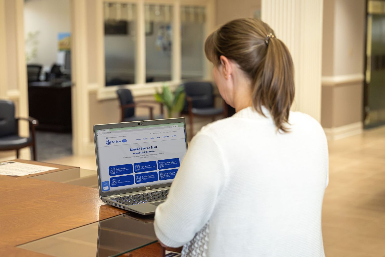 PSB Bank employee using a laptop displaying the PSB Bank website inside a bank branch.
