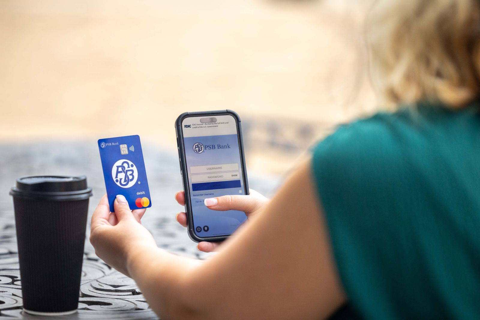 Person holding a PSB Bank debit card and smartphone displaying the PSB Bank mobile banking login screen.