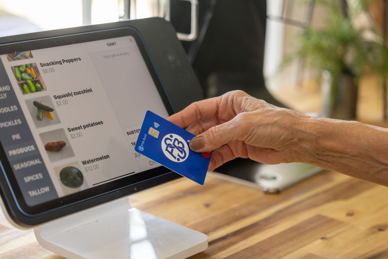 Hand holding a PSB Bank debit card near a point-of-sale terminal during a retail purchase.